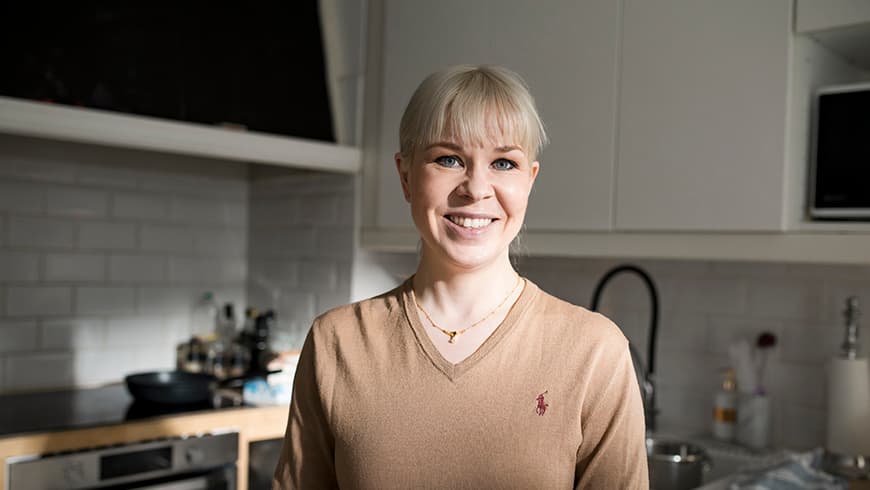 Nuori nainen hymyilee iloisesti keittiössä.