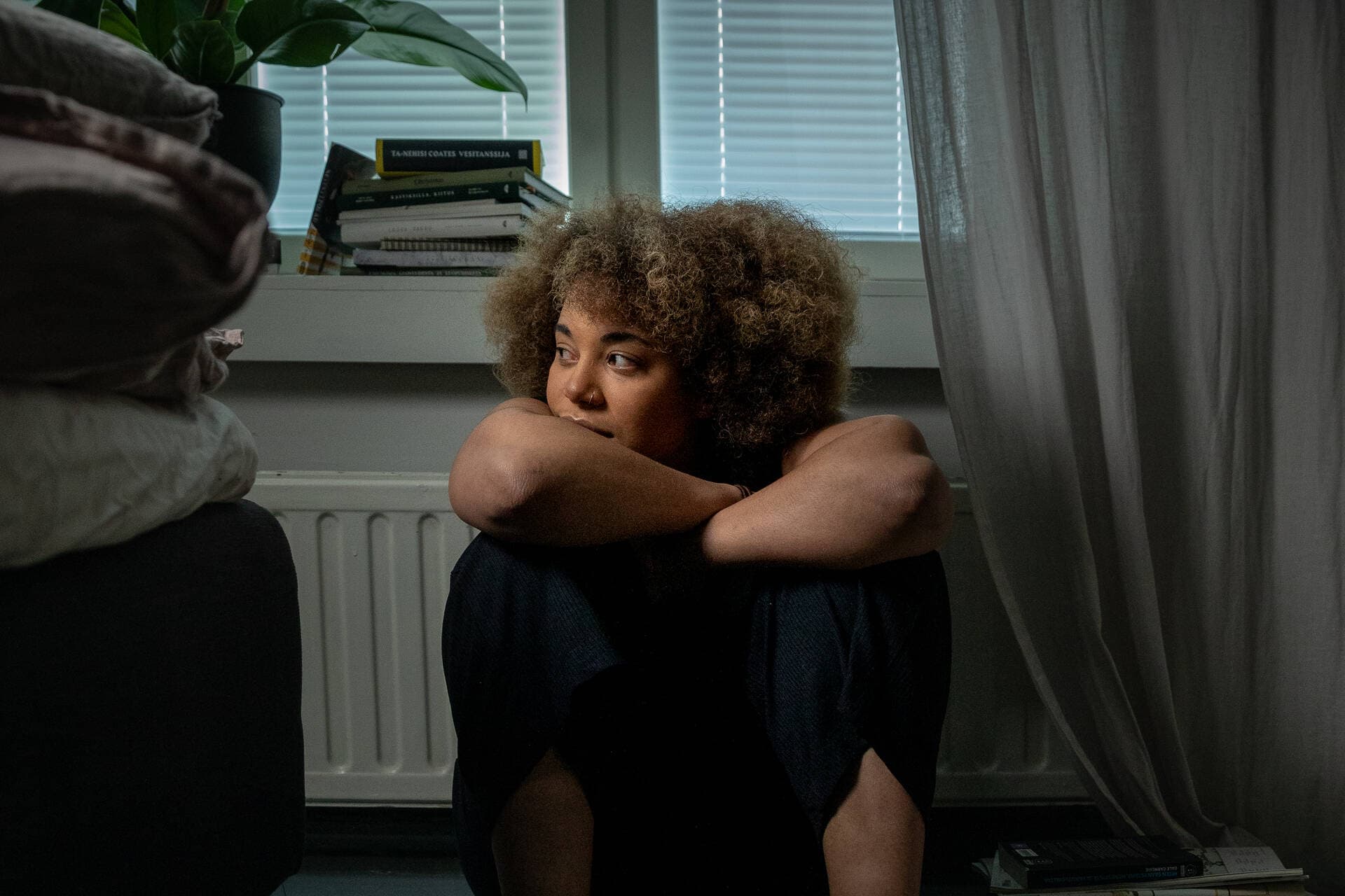 A person sitting on the floor and leaning against a radiator while pondering.