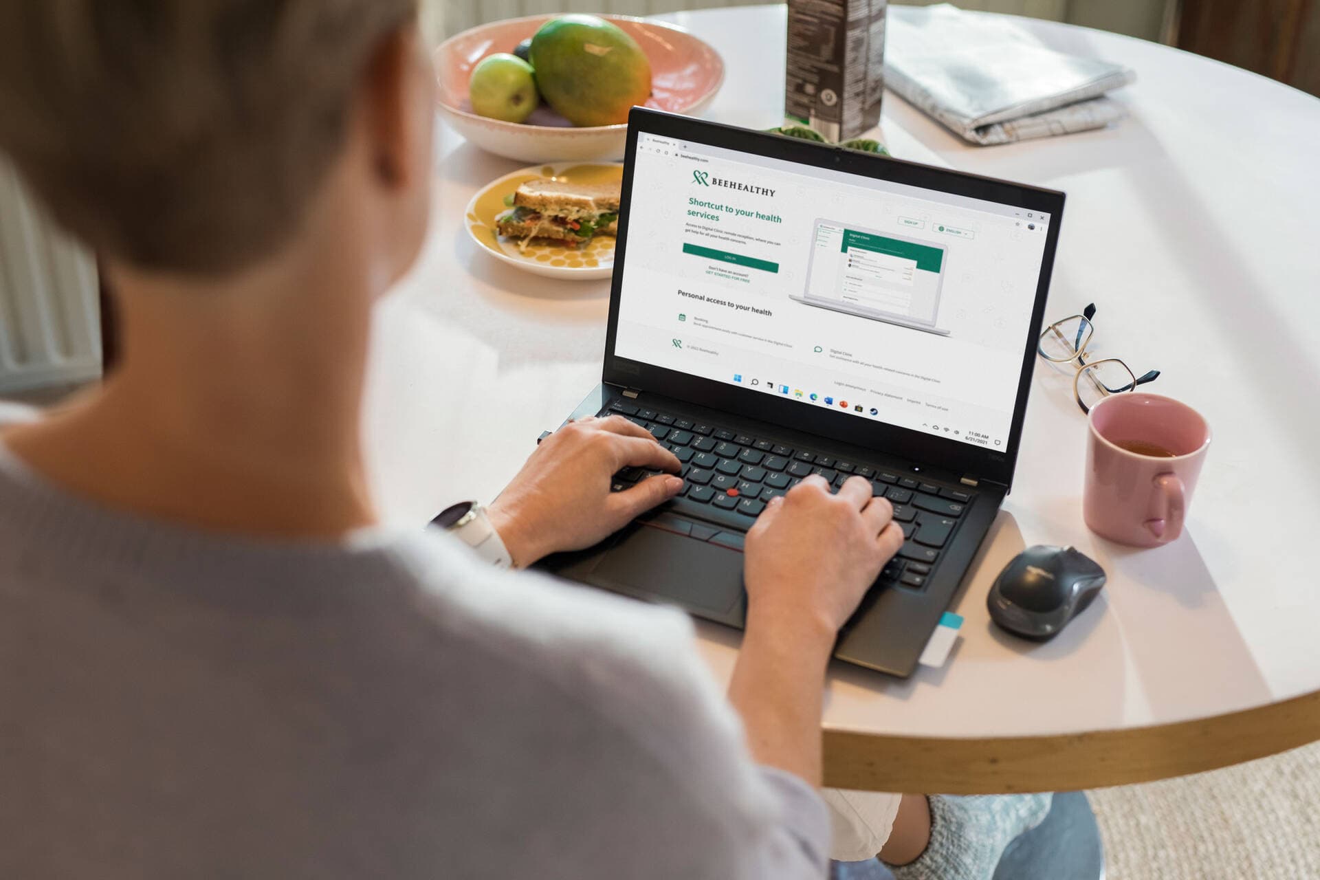 A person is sitting at the dining table browsing the BeeHealthy website on a laptop.