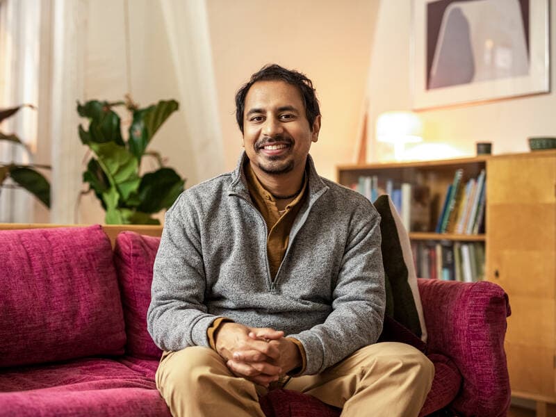 A man sits on the living room sofa, smiling.