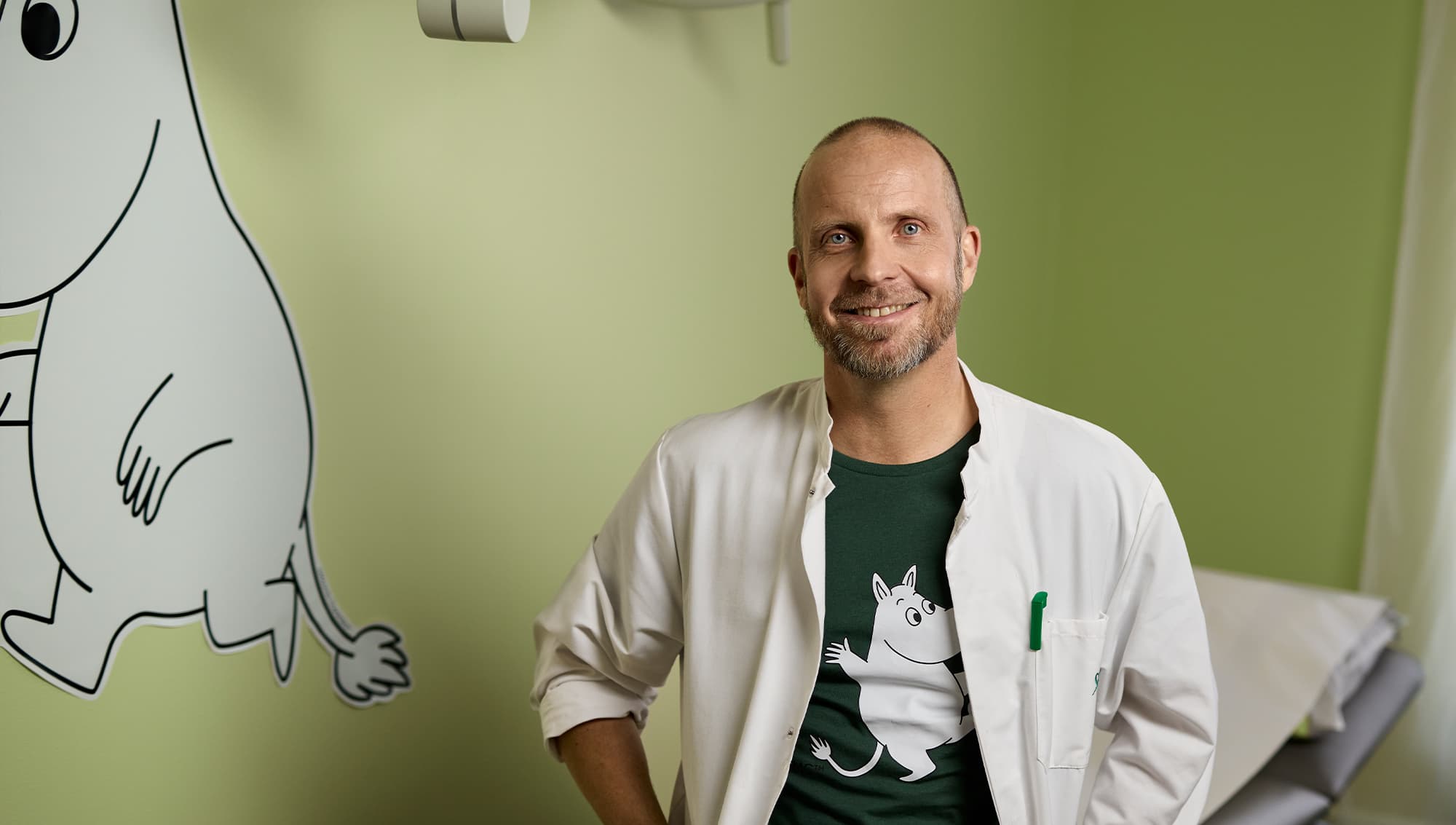 Mehiläisen lastenlääkäri Petri Koponen istuu vastaanottohuoneessa ja katsoo lempeästi kameraan