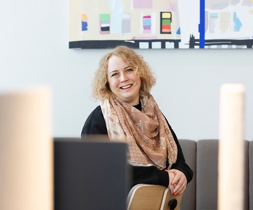 A blonde woman sits on the sofa and smiles. Laura Tero Gofore.